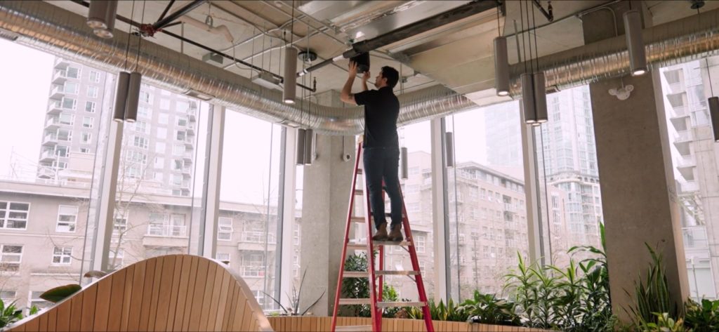 Pure Image technician installing a Sonance speaker in a commercial space, with the system backend powered by Sonos for seamless audio integration