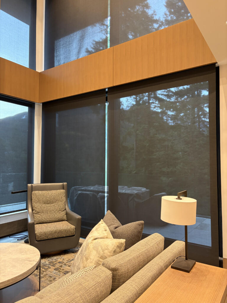 Timber-lined lounge with Lutron shades lowered across the windows, forest visible beyond