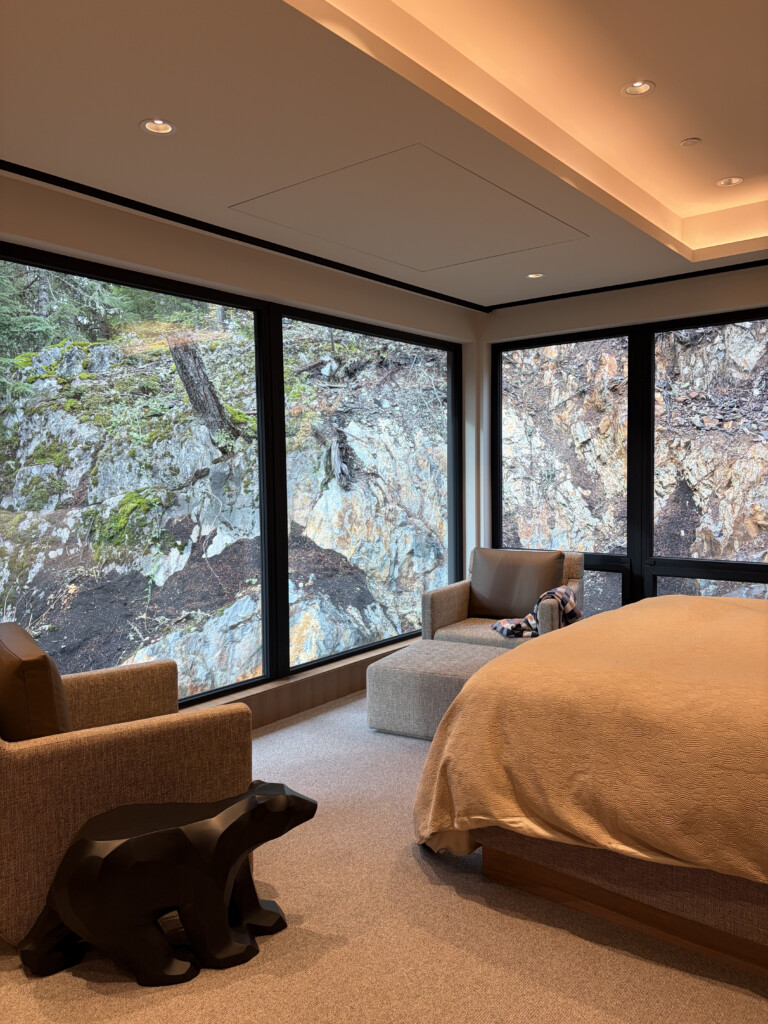 Luxury Whistler chalet bedroom with Lutron recessed lighting, cove lighting and floor-to-ceiling windows overlooking natural rock face — Pure Image smart home lighting installation Whistler