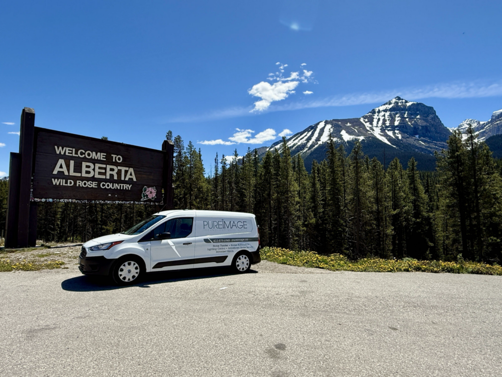 Pure Image van parked at the Welcome to Alberta sign, with the Rockies behind