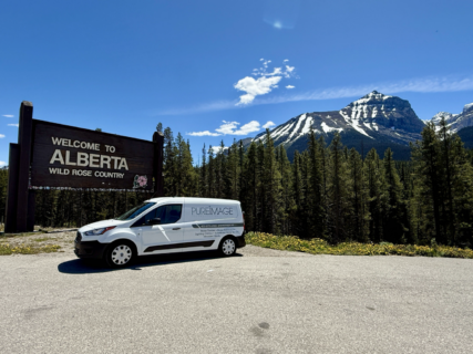Pure Image van parked at the Welcome to Alberta sign, with the Rockies behind
