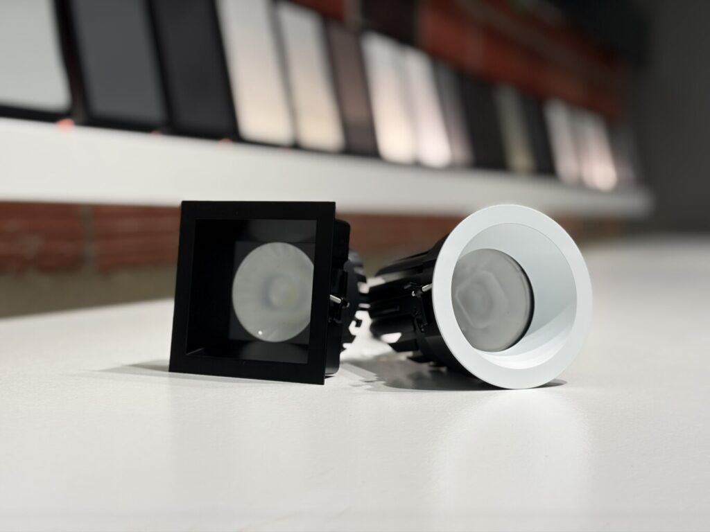 Square black and round white Ketra D2R downlight trims on a showroom counter, shade fabric samples behind
