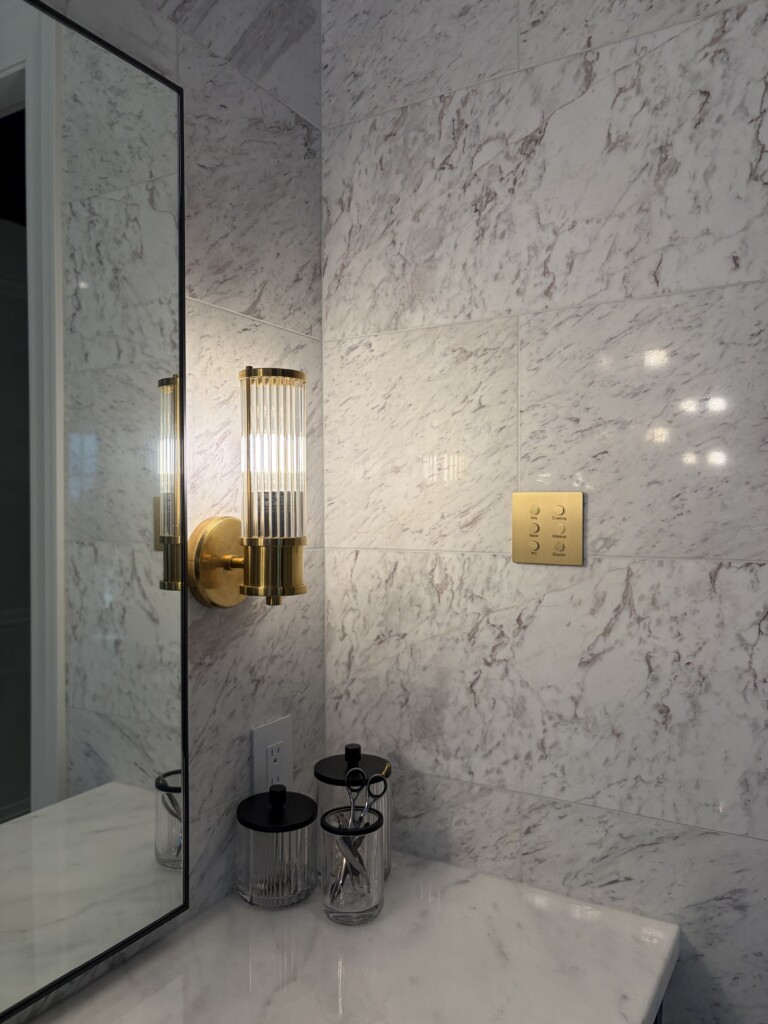 Lutron Alisse keypad in brushed brass controlling scene lighting and shades in a marble bathroom, installed by Pure Image.