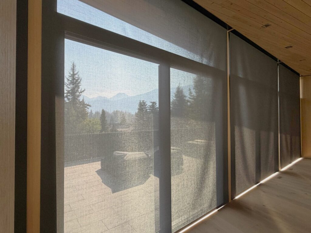 Lutron light-filtering roller shades on floor-to-ceiling windows with a mountain view in Whistler, installed in a private residence by Pure Image.