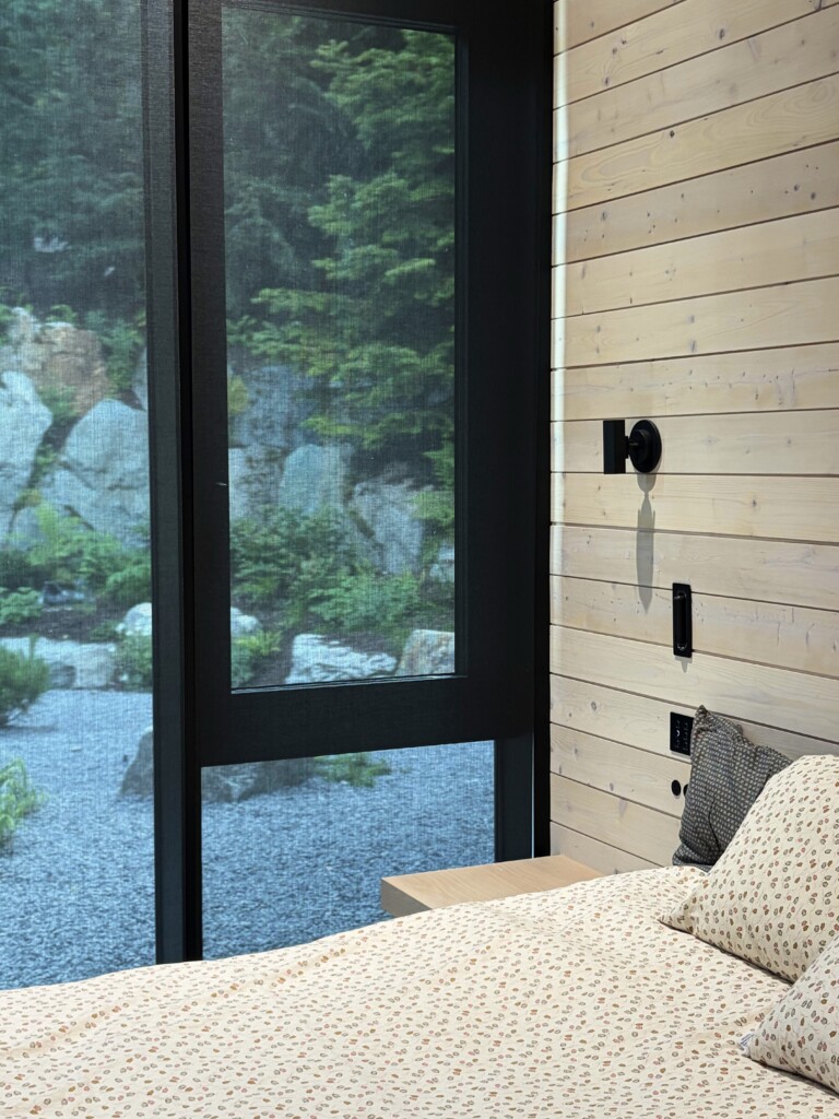 Lutron light-filtering roller shade partially lowered over a bedroom window with a forest view, installed in a private residence by Pure Image.