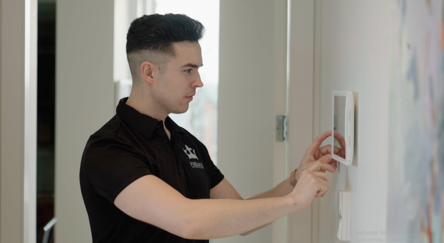 Pure Image technician operating a wall-mounted touchscreen control panel in a luxury residence