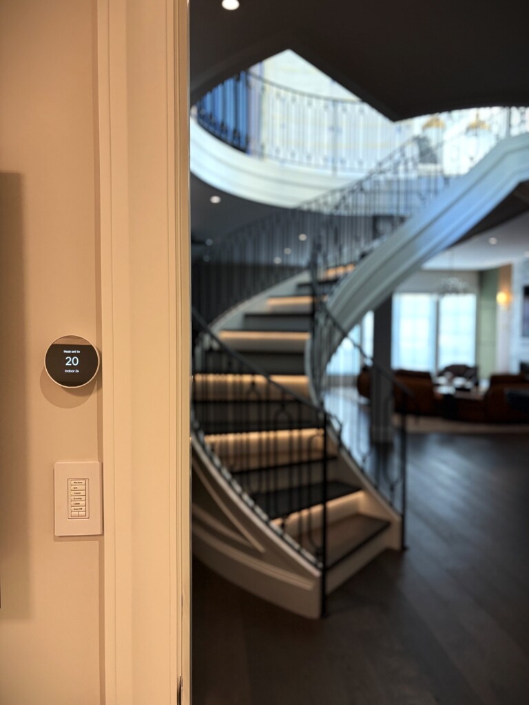 Lutron seeTouch keypad and smart thermostat by a curved staircase in a luxury home, installed by Pure Image for lighting and climate control.