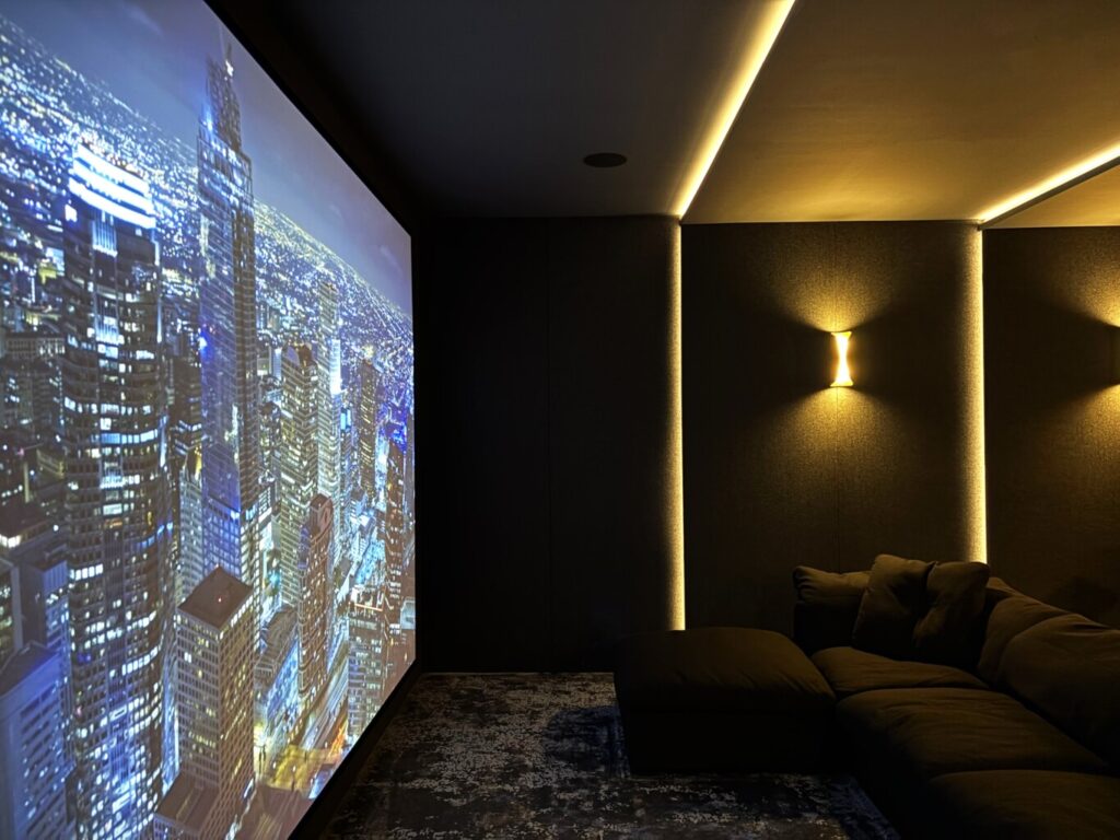 Immersive home theatre with a floor-to-ceiling projection screen and ambient wall lighting, custom built by Pure Image.