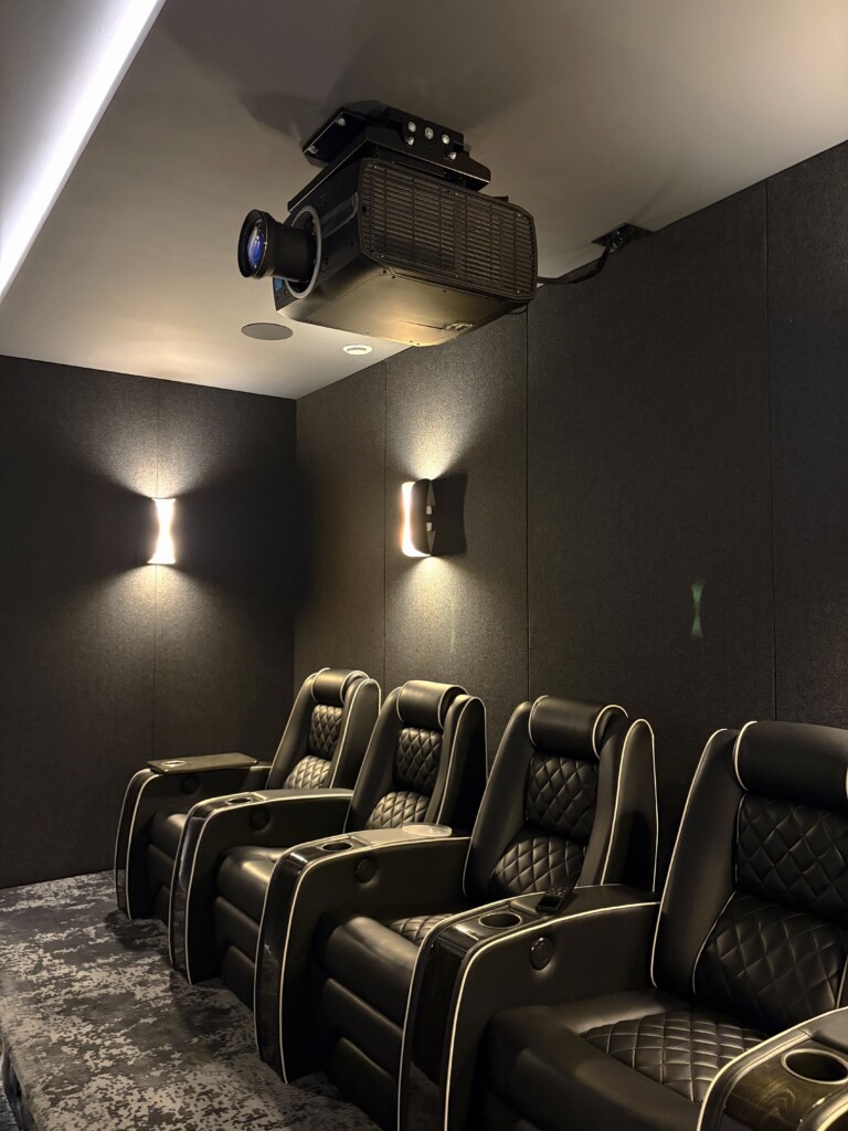 Ceiling-mounted cinema projector above premium leather recliner seating in a custom home theatre by Pure Image.