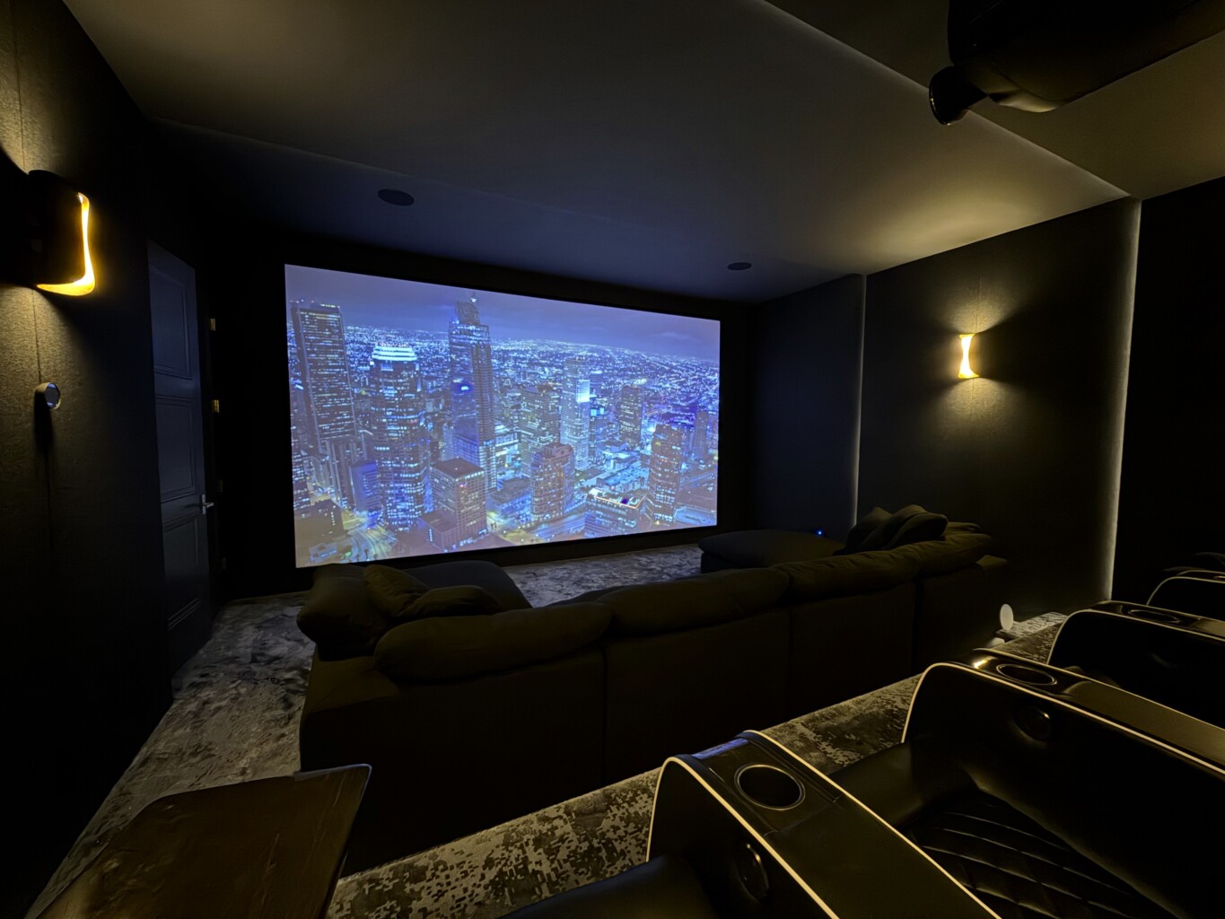 Luxury home cinema room with a large projection screen, tiered seating, and acoustic wall panels, designed and installed by Pure Image.