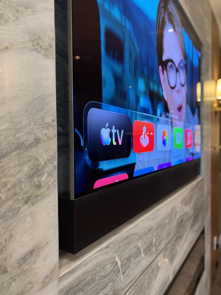 Wall-mounted TV with an integrated soundbar on a marble feature wall, showing the Apple TV interface, installed by Pure Image.