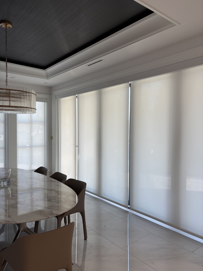 Motorized roller shade fully lowered across a dining room window, offering privacy and daylight at the same time, designed and installed by Pure Image Technology